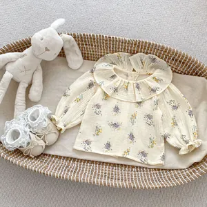 Detail of floral baby blouse with ruffled collar and elastic cuffs on beige fabric