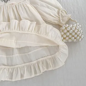 Detailansicht von besticktem Kragen und Rüschensaum an diesem cremefarbenen Mädchenkleid
