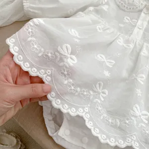 Dettaglio di un body bianco per neonati con ricamo traforato e chiusura a scatto