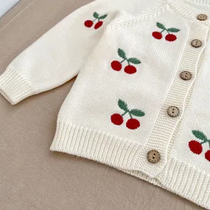 Dettaglio del cardigan in maglia per neonati con ciliegie ricamate e bottoni in legno