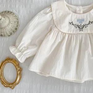 Detail der beige Mädchenbluse mit Blumenstickerei und blauer Schleife am Peter-Pan-Kragen