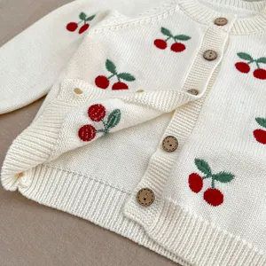 Dettaglio del cardigan in maglia per neonato con ricami a ciliegia e bottoni in legno