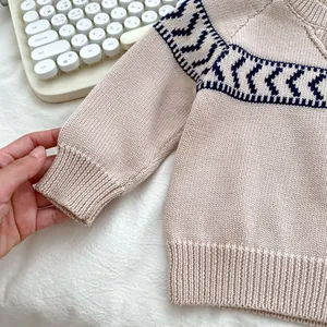 Detail of baby boy knitted sweater showing ribbed cuffs and navy herringbone patterns