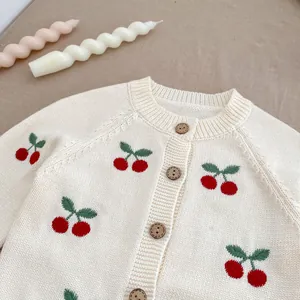 Dettaglio del cardigan crema per neonati con ricamo a ciliegia e bottoni marroni