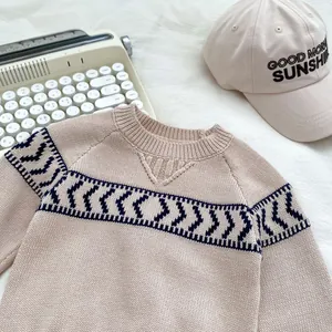 Close-up of beige knit sweater featuring blue geometric patterns and ribbed crew neck details