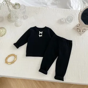 Detail eines gerippten Baby-Langarm-Sets mit süßen weißen Schleifen auf schwarzem Stoff