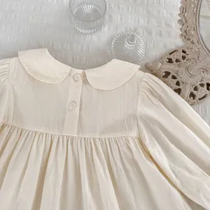 Detail eines cremefarbenen Langarm-Babyshirts mit Bubikragen und feinen Rüschen