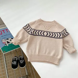 Detailed view of beige knitted baby sweater with navy geometric patterns and ribbed collar