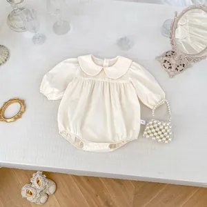 Détail du body bébé crème avec col Claudine et manches bouffantes sur parquet en bois