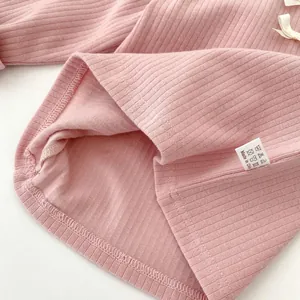 Detail von rosa geripptem Baby-Strickshirt mit weißer Schleife und weichem Saum