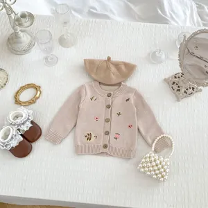 Dettaglio del cardigan in maglia rosa con ricami floreali e bottoni in legno per neonati