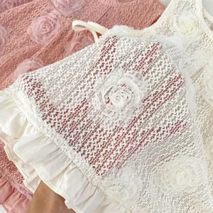 Détail de robe bébé avec appliqués de roses 3D, dentelle ajourée et volants souples