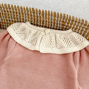 Detail eines rosa Baby-Strickstramplers mit cremefarbenem Häkelkragen und Knopf