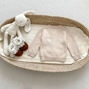 Cardigan in maglia per neonati beige con ricami floreali in un cesto di vimini