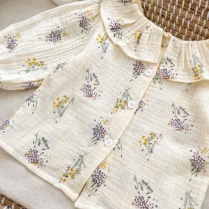Close-up of baby floral muslin blouse with ruffled collar and delicate wooden buttons