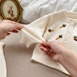 Détail d'un cardigan en tricot pour bébé avec broderie carotte et boutons blancs