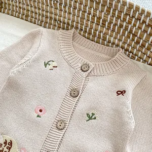 Dettaglio del cardigan in maglia rosa per neonato con ricami e bottoni in legno