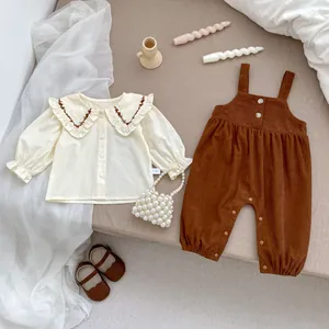 Baby-Herbstoutfit mit Rüschenkragenhemd und Cord-Latzhose auf beigefarbenem Stoff