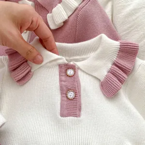 Close-up of pink ruffled collar and gold-trimmed buttons on a white knit girls' dress