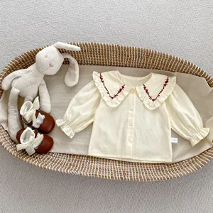 Detailansicht der Babybluse mit Spitzenkragen, roter Stickerei und weißen Knöpfen