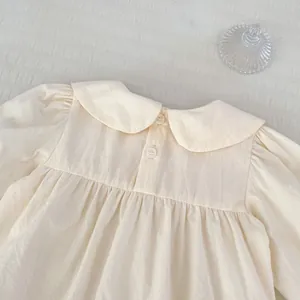 Détail d'un body bébé en coton beige avec col Peter Pan et fermeture boutonnée au dos