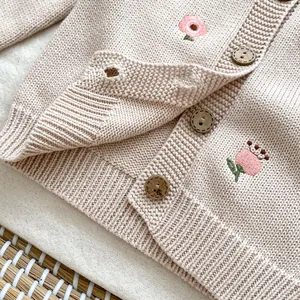 Dettaglio del cardigan in maglia per neonati con ricami floreali rosa e bottoni in legno