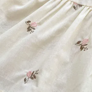 Dettaglio di pagliaccetto per neonati con ricamo di fiori rosa e trama plissettata
