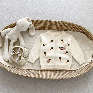 Détail du cardigan tricoté pour bébé avec broderie de carotte et lapin blanc crème