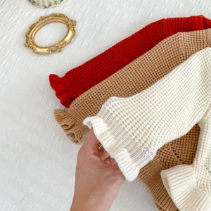 Detalle de jerséis de punto de gofre con puños con volantes en rojo, caqui y crema
