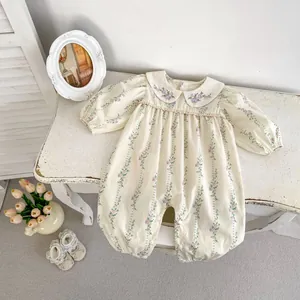 Floral baby girl romper with embroidered collar and long sleeves on a vintage bench