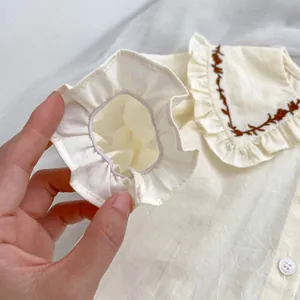 Detail von Rüschenmanschetten und Stickerei auf gelbem Babyhemd mit Blättermuster-Kragen