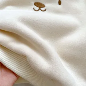 Gros plan d'un sweat en polaire crème avec broderie ours et finitions en bord-côte