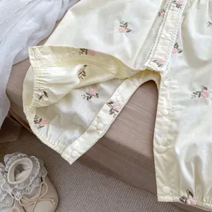 Dettaglio di pagliaccetto per neonato con ricami floreali e pizzo bianco su tessuto crema
