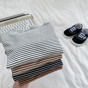 Close-up of stacked striped cotton baby t-shirts in various neutral tones on white bedding