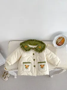 Detailed view of girl's quilted winter jacket with floral embroidery and green frilled collar