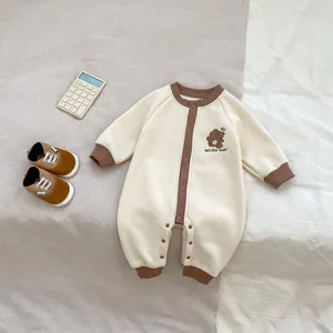 Détail d'une grenouillère bébé crème avec bordure en tricot marron et broderie ours