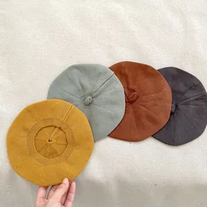 Detail of four knitted baby berets in mustard yellow, green, rust red, and grey wool fabric