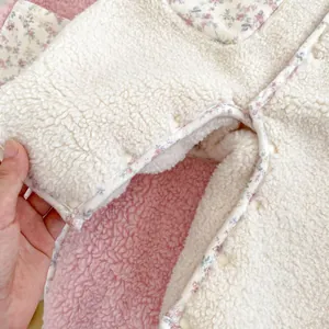 Close-up of baby romper showing soft lamb wool fabric, floral trim and resin snaps
