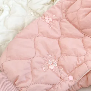 Detail of pink quilted infant romper with floral embroidery and resin snap buttons