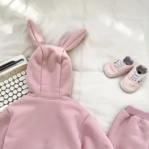 Flat lay of pink baby girl winter tracksuit with 3D bunny ears and matching canvas shoes