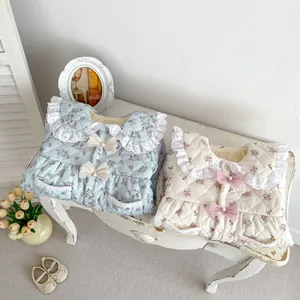 Close-up of quilted floral vests with lace collars and bows on a white bench