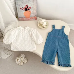 Détail d'une chemise blanche brodée à volants et d'une salopette en jean pour bébé