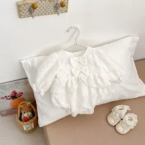 Detail of white infant bodysuit with quilted embroidery, lace trim, and matching soft shoes