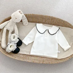 Detailansicht des weißen Baumwolloberteils für Babys mit Rüschenkragen und Etikett