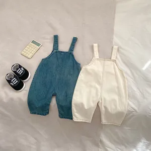 Salopettes en jean pour bébé et barboteuses beige posées sur un tissu texturé naturel