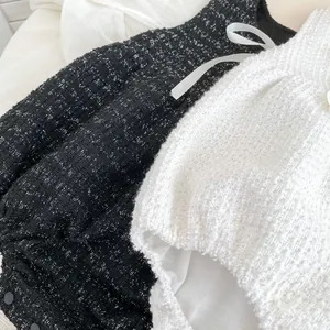 Nahaufnahme der Tweed-Textur und der weißen Bandschleife an Neugeborenen-Bodys