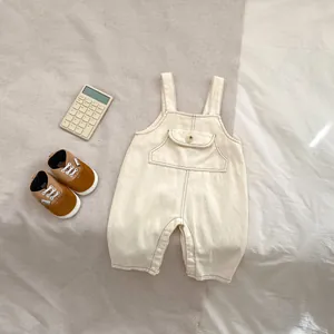 Détail de la salopette en denim beige pour bébé avec poche poitrine et boutons pressions