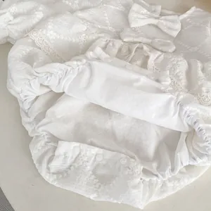 Detail of white cotton baby romper featuring floral embroidery and lace trim textures