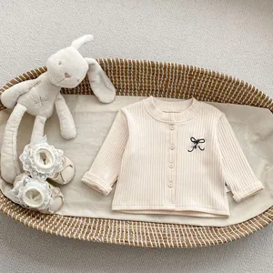 Detail of baby knitted cardigan with wood buttons and black bow embroidery in a woven basket