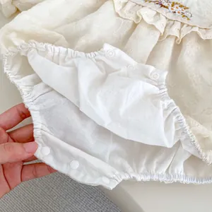 Detail of snap button closures and floral embroidery on off-white baby romper